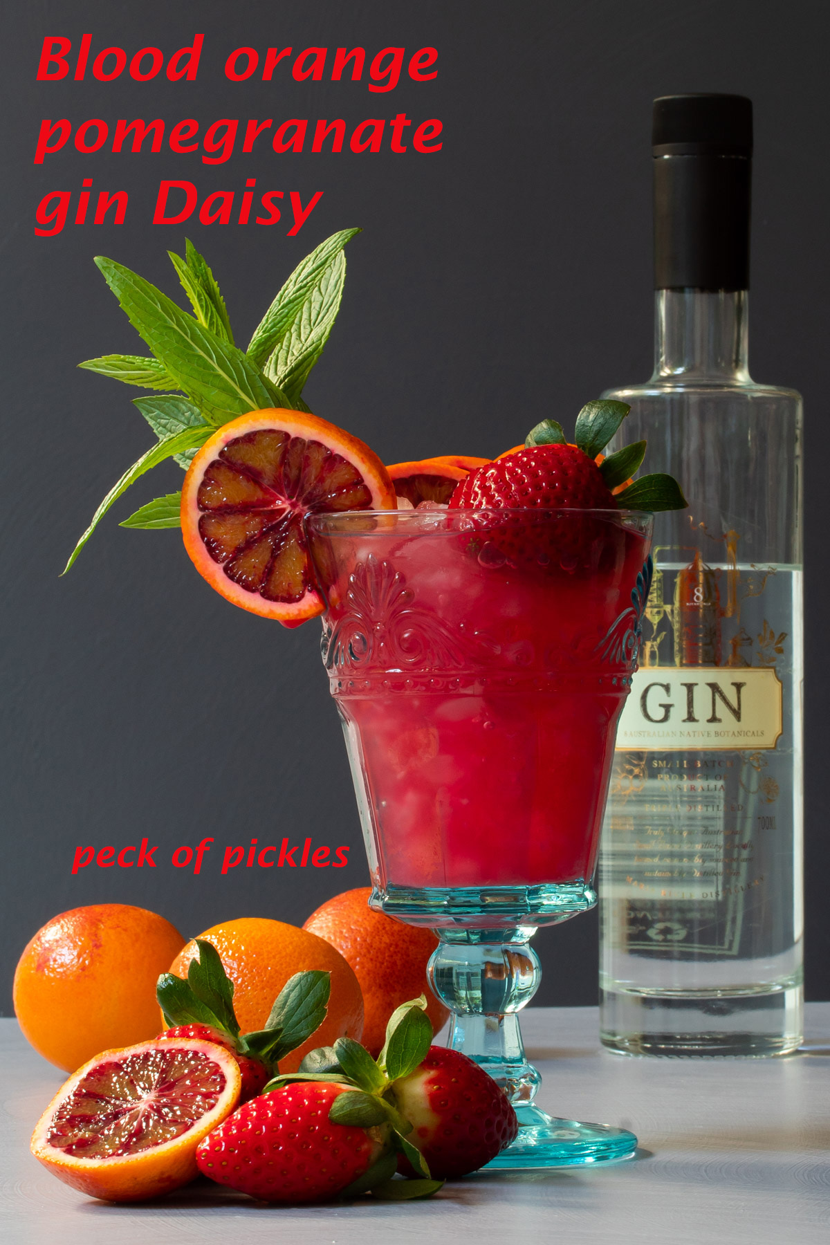 blood orange pomegranate gin daisy cocktail with fruit in foreground and gin bottle in background