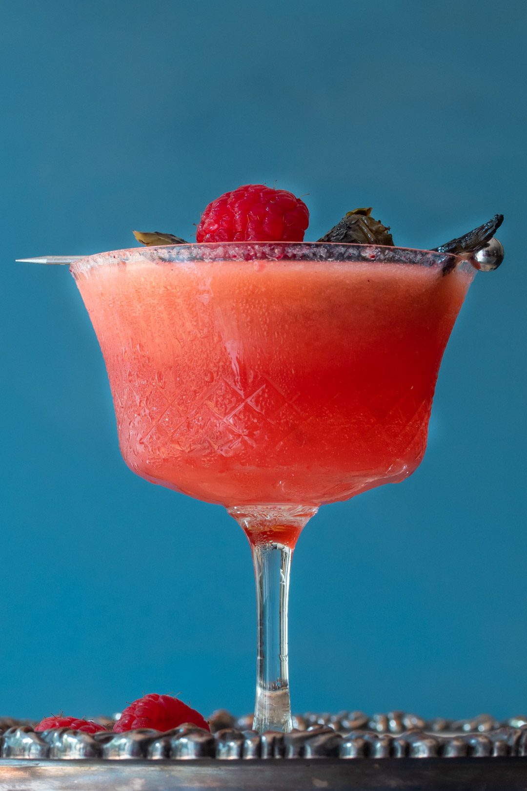 Pickled jalapeno and raspberry margarita cocktail with hibiscus sugar: blue background