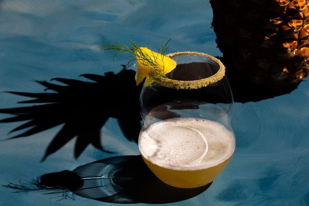 pineapple fennel shrub margarita cocktail with pineapple and shadow closely framing glass