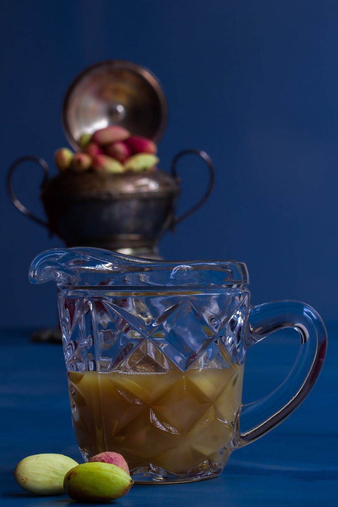 pistachio rose water orgeat syrup in cut glass antique jug with fresh pistachios in foreground and background