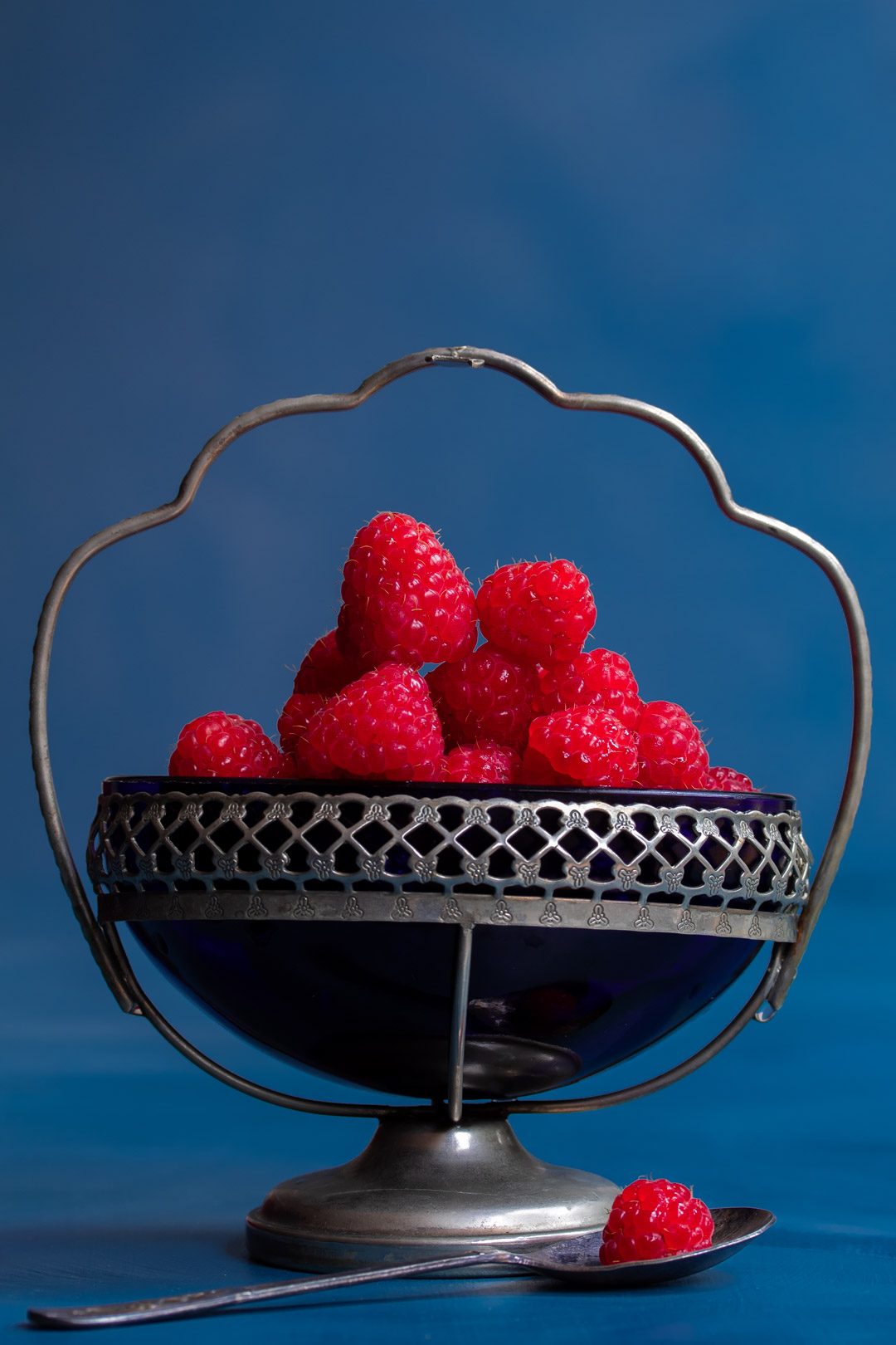 Making Raspberry shrub syrup drinking vinegar with raspberries in vintage blue glass sugar bowl with raspberry in sugar spoon in foreground