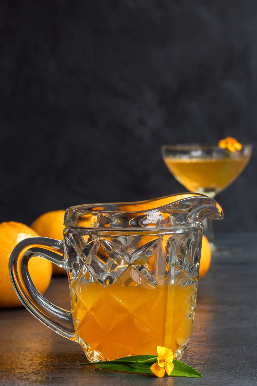 Mandarin tarragon shrub syrup drinking vinegar in vintage glass jug with cocktail in background