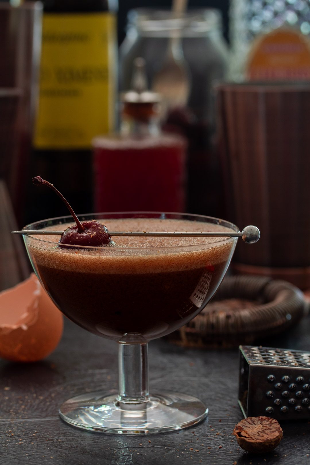 Pickled cherry chocolate sherry flip cocktail with bottles in background