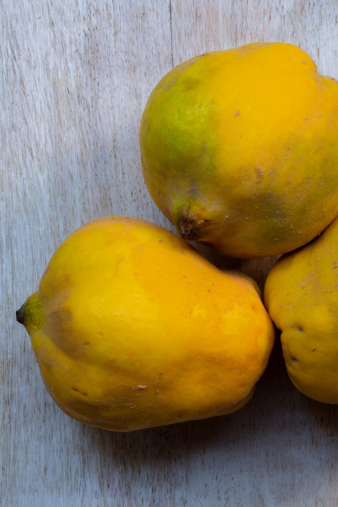 Making Spiced pickled quinces with 2 quinces on white background, third partially in frame