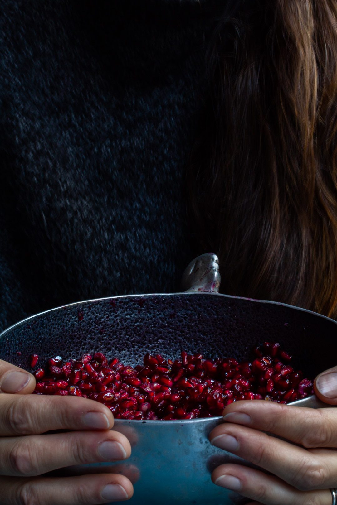 hands holding a metal bowl of pomegranate arils used to make grenadine