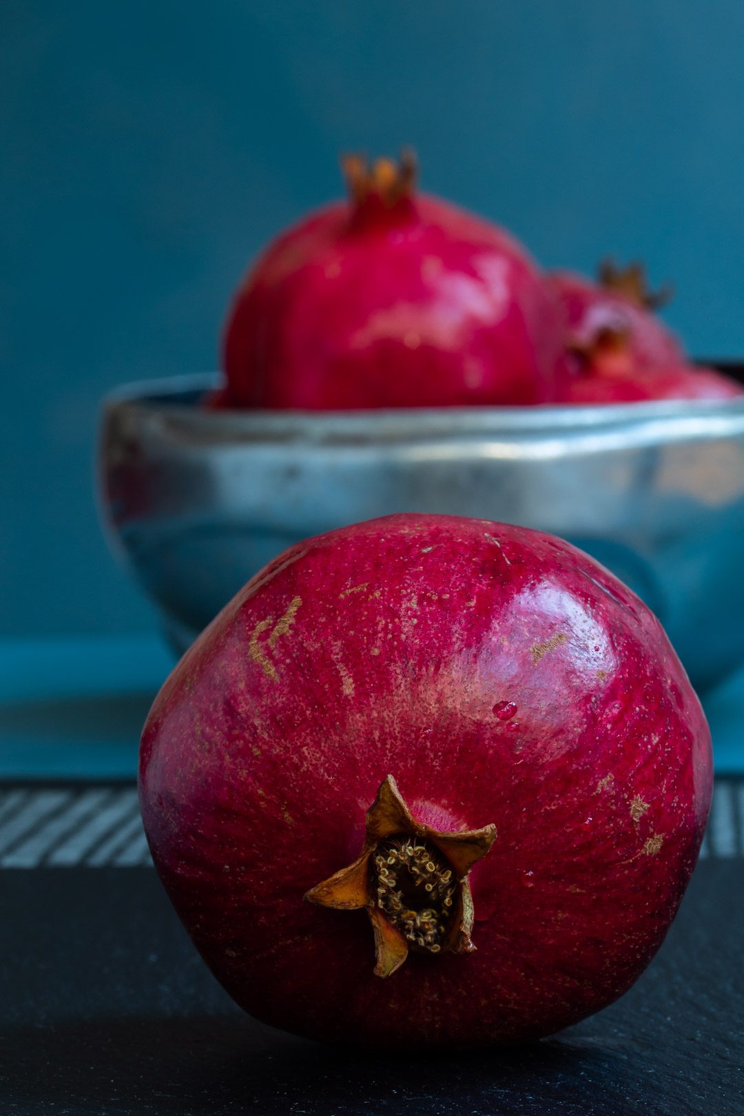 pomegranate face on with metal bowl of pomegranates in background used to make grenadine