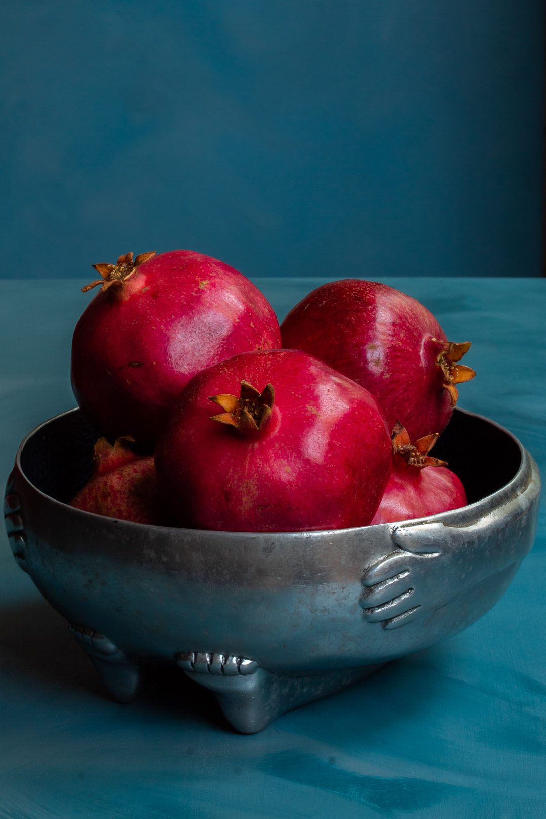 pomegranates in metal bowl used to make grenadine on blue background