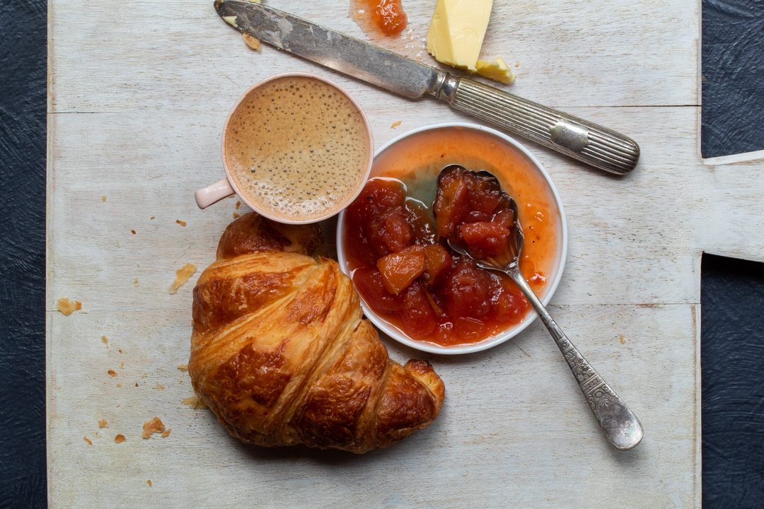 rustic quince apple jam with croissant and coffee on white chopping board