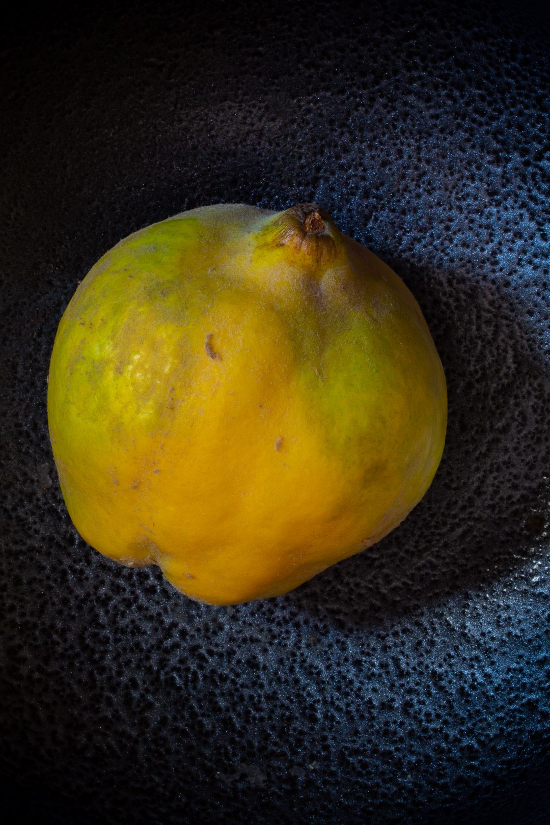 Making Spiced pickled quinces with single quince on black metallic background