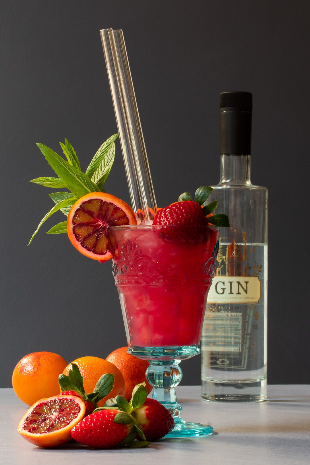 blood orange pomegranate gin daisy cocktail with bottle in background and fruit in foreground