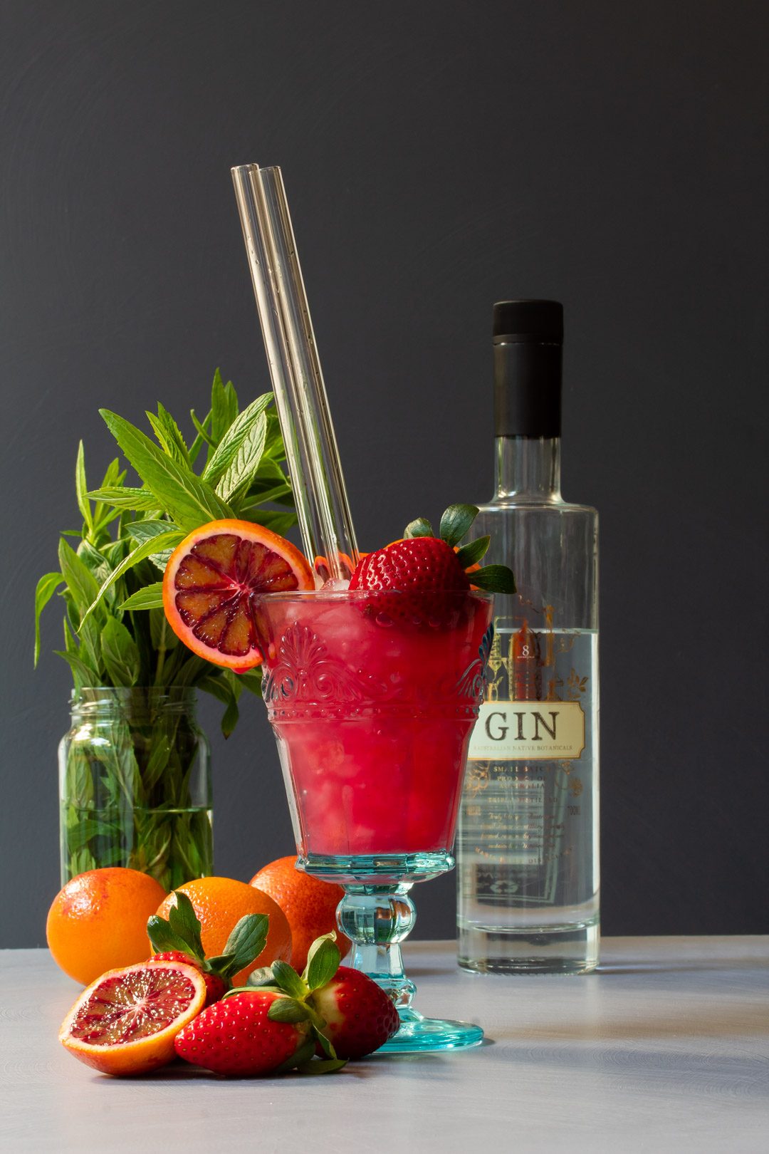 blood orange pomegranate gin daisy cocktail with mint and gin bottle in background