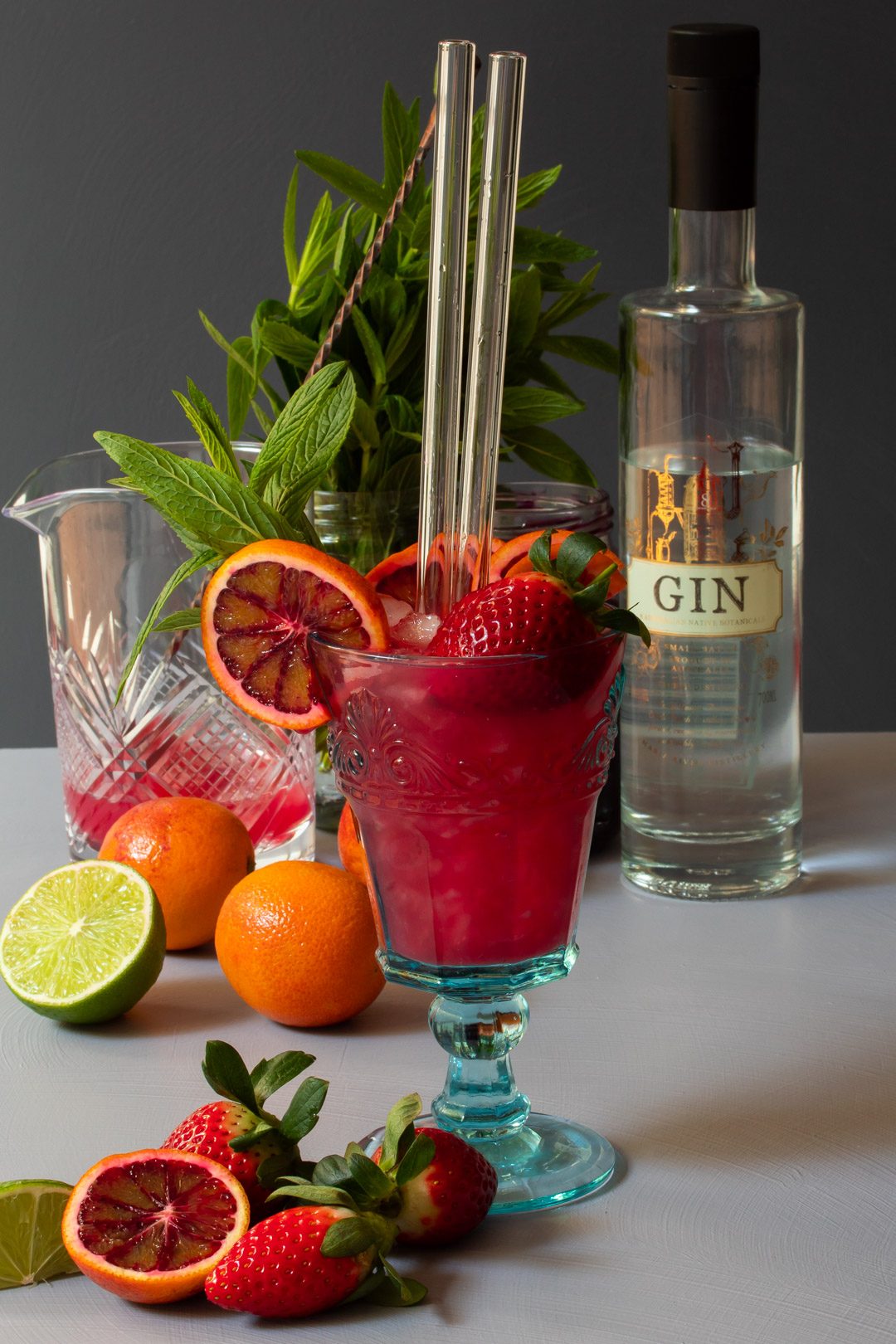blood orange pomegranate gin daisy cocktail with mixing glass, fresh fruit, gin bottle, mint from 45 degrees