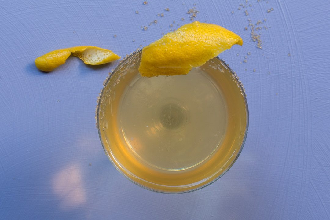 Fancy quince brandy champagne cocktail from above with lemon twist on light purple background