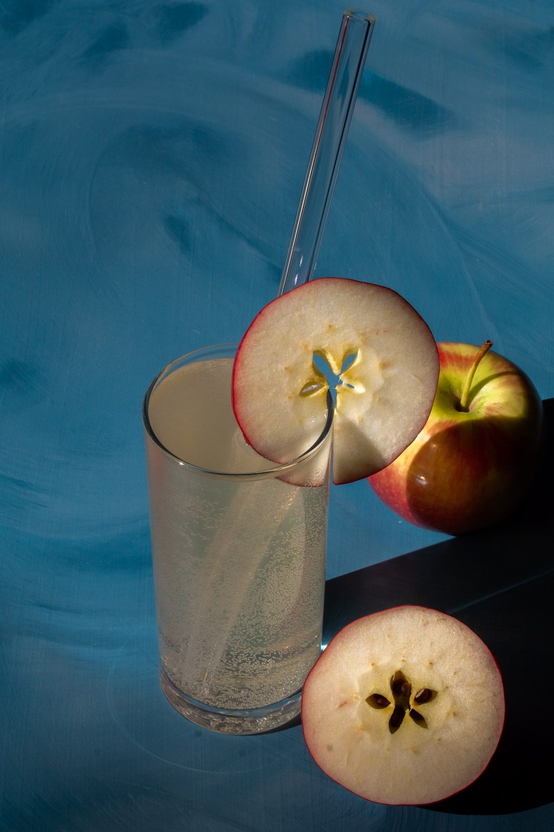 apple shrub gin fizz cocktail from 45 degrees on blue background with apples