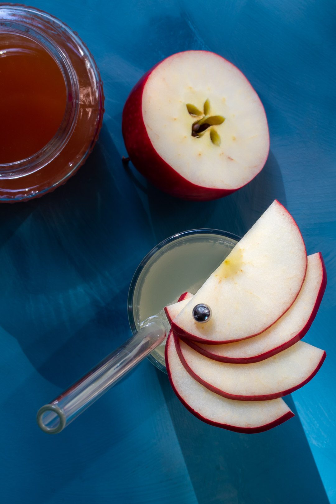 apple shrub gin fizz cocktail from above with apple fan garnish, cut apple and shrub syrup