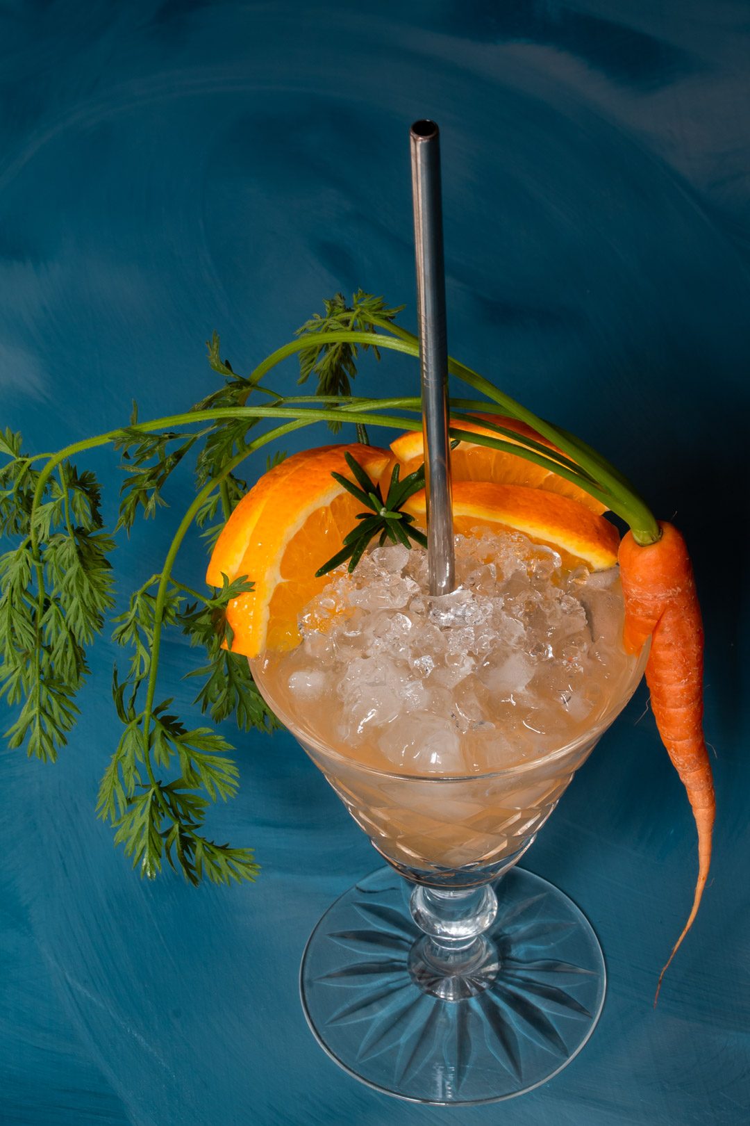 carrot shrub daisy cocktail from 45 degree angle on a blue textured background