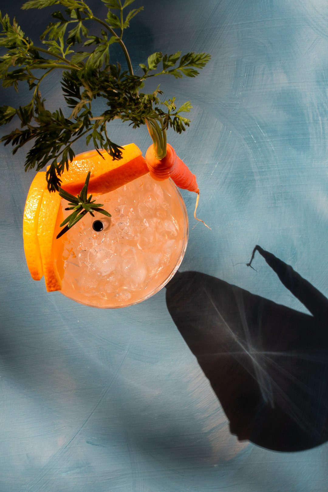 Carrot shrub daisy cocktail from above on blue background with shadows and hard light