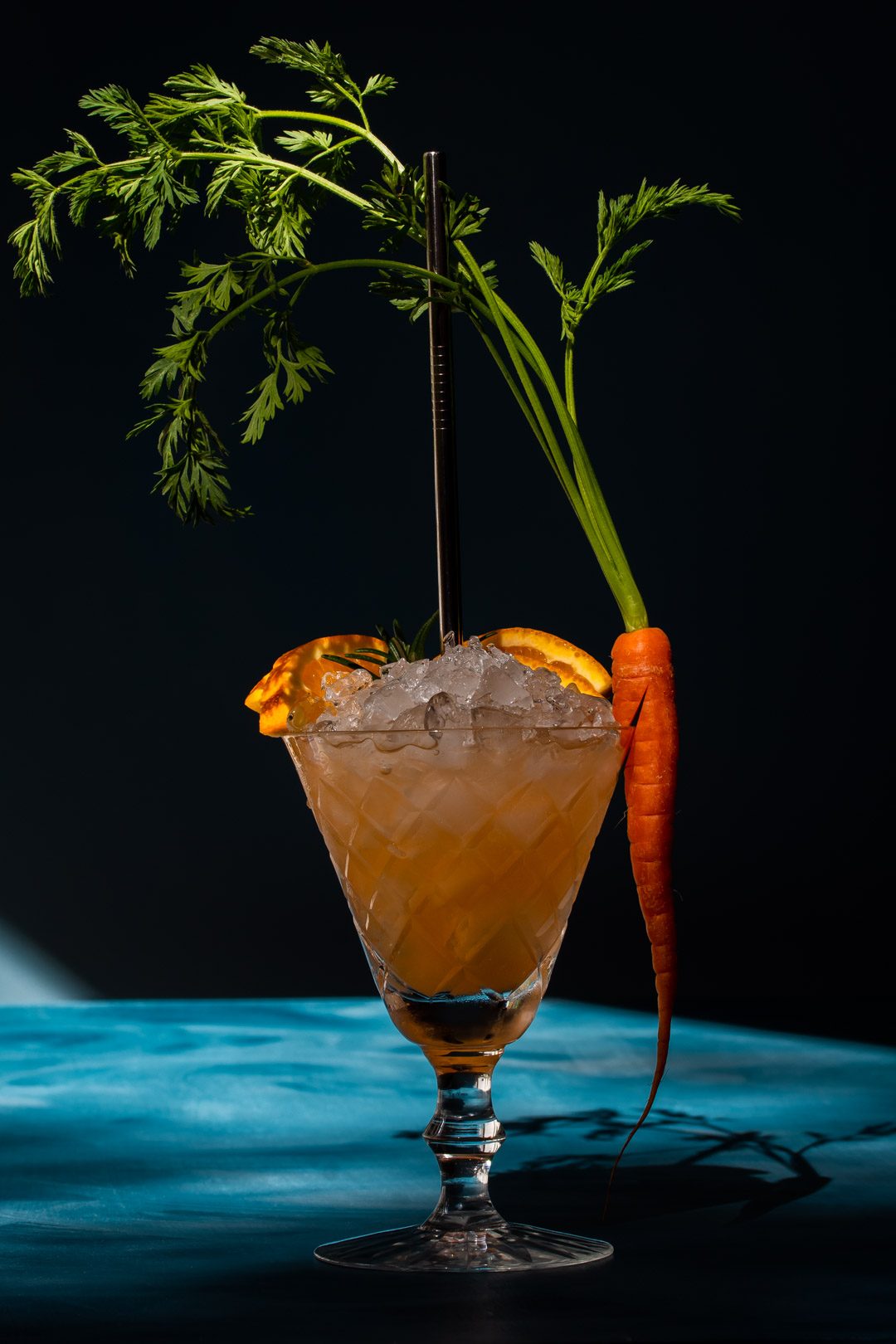 carrot shrub daisy cocktail with deep shadows on blue background