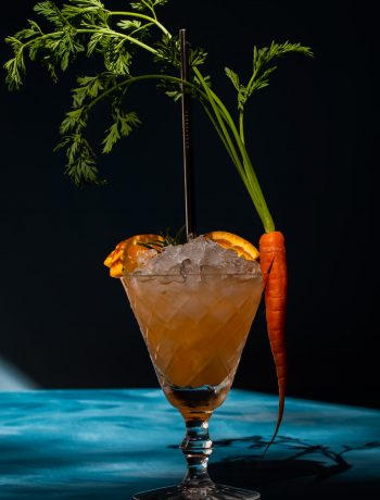 carrot shrub daisy cocktail with deep shadows on blue background