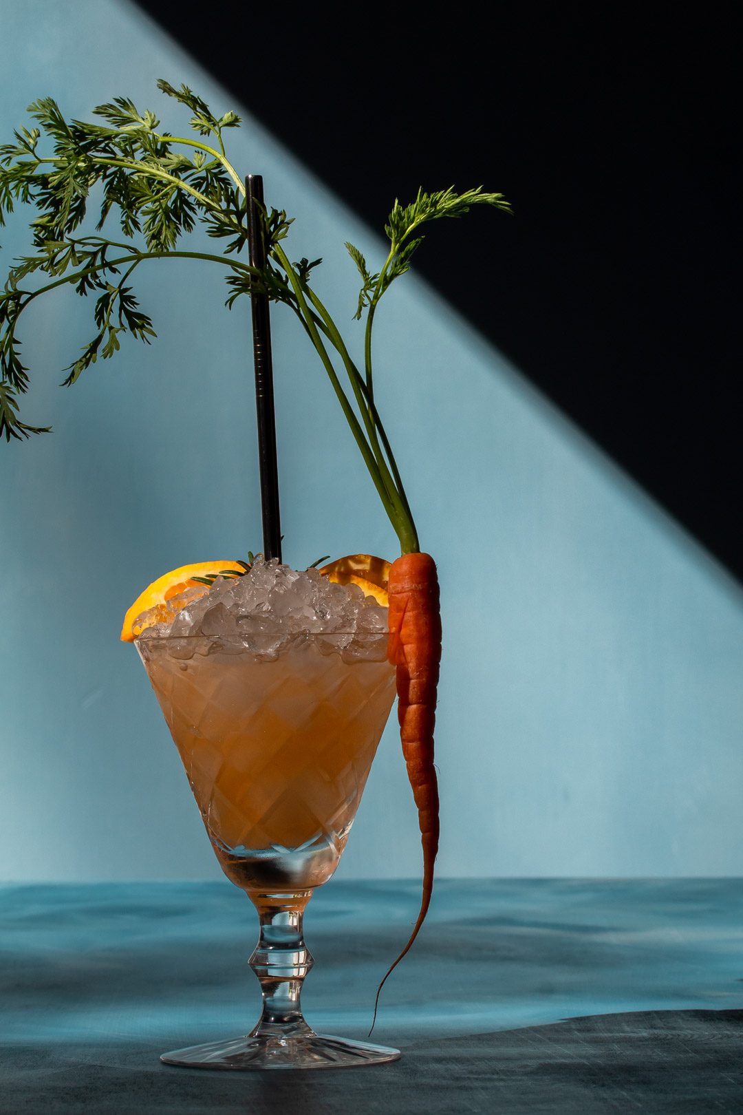 carrot shrub daisy cocktail with shadows to right on blue background