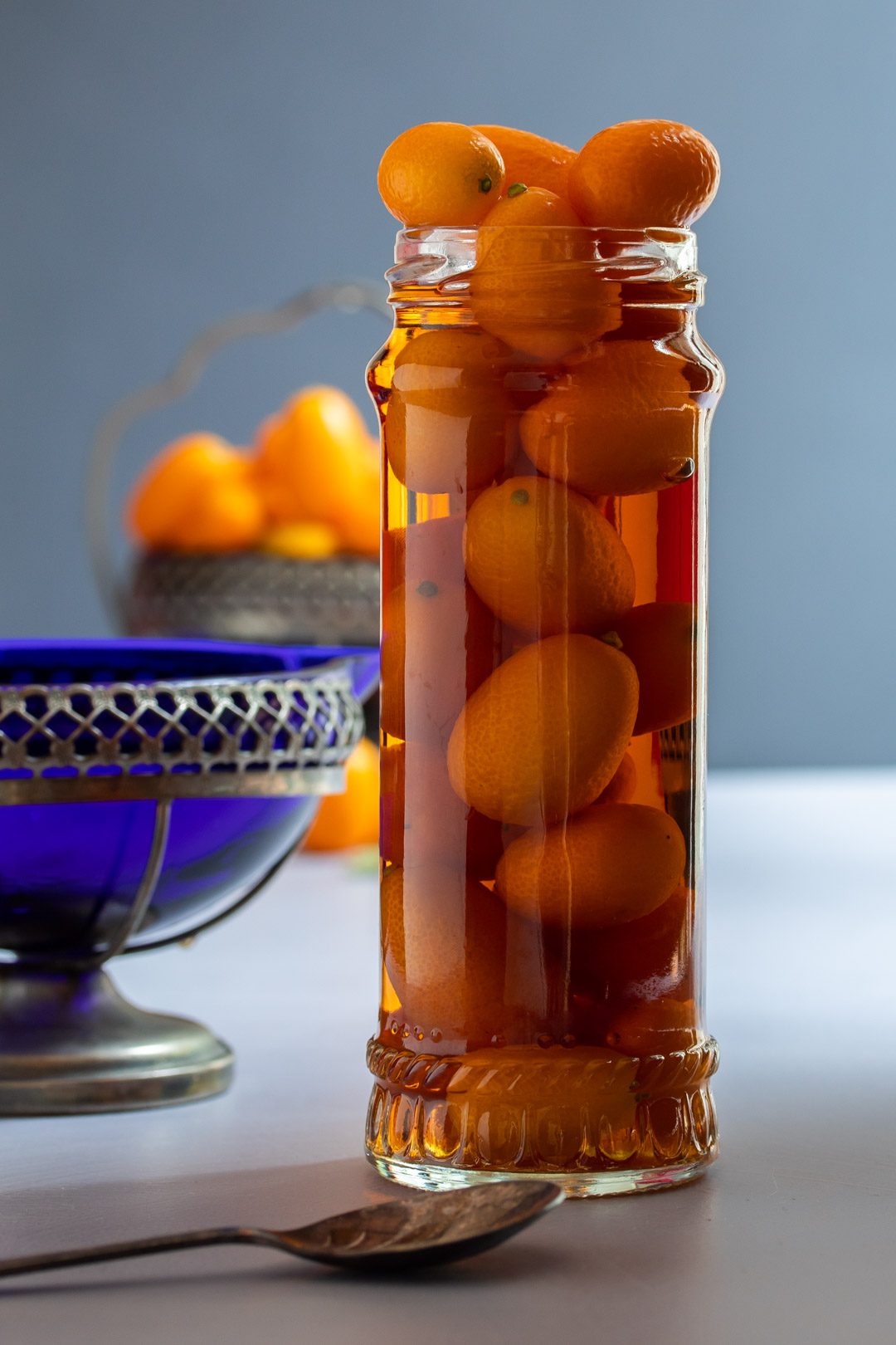 cumquat brandy with blue glass jug and dish of cumquats in background