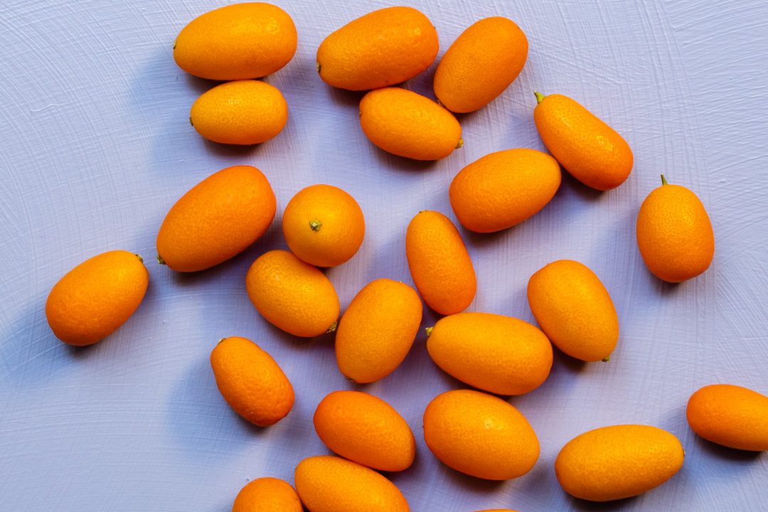 making cumquat brandy with cumquats on light purple background