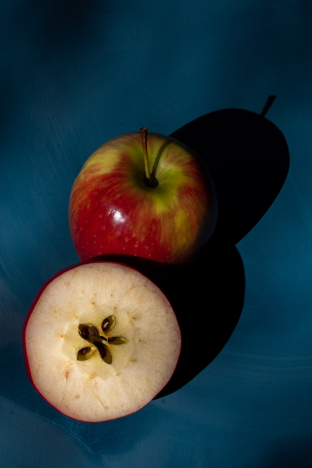 making an apple shrub gin fizz cocktail with cut apple and whole apple in hard light with shadows