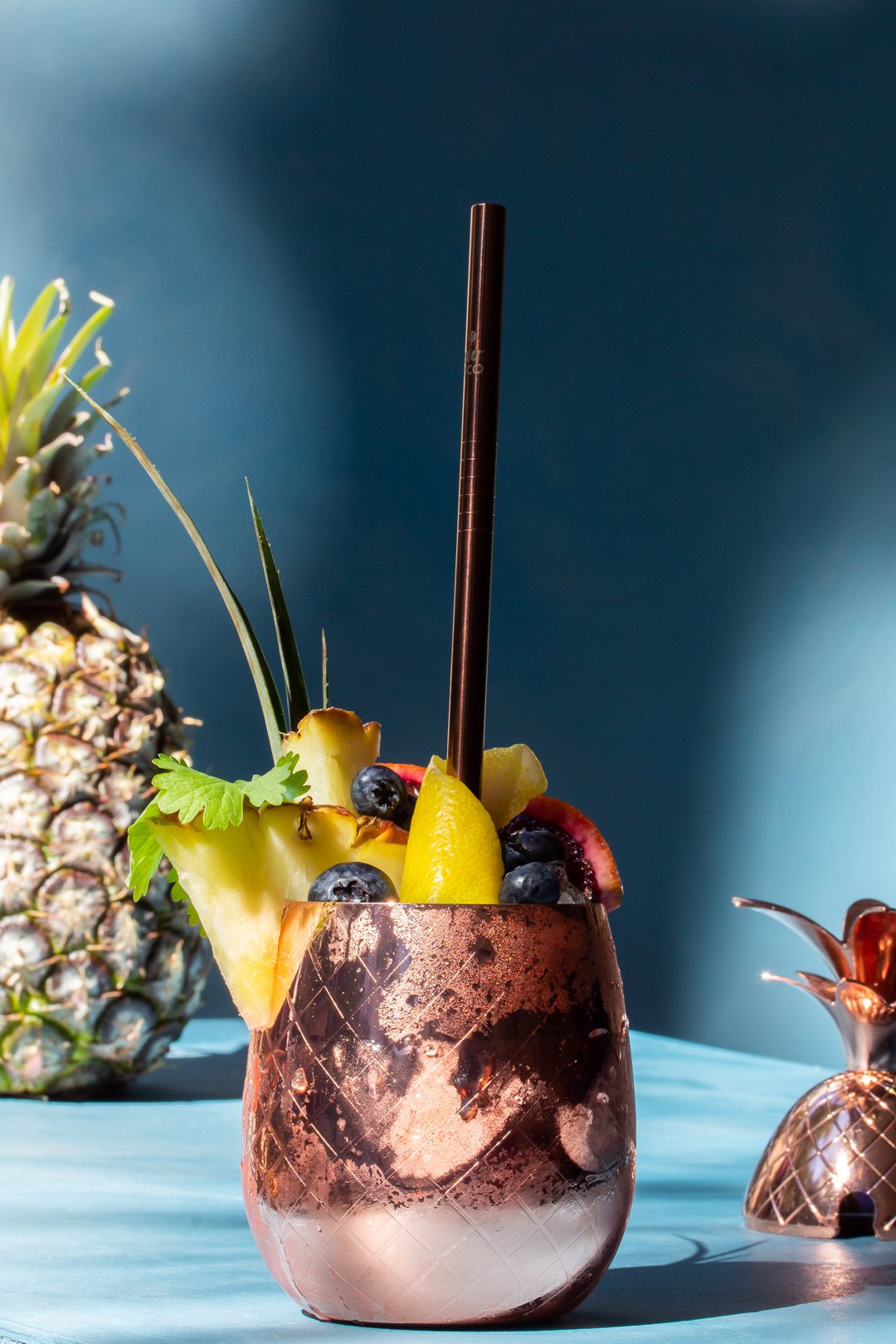 pineapple shrub gin fix cocktail with pineapple i n background and pineapple lid to right foreground