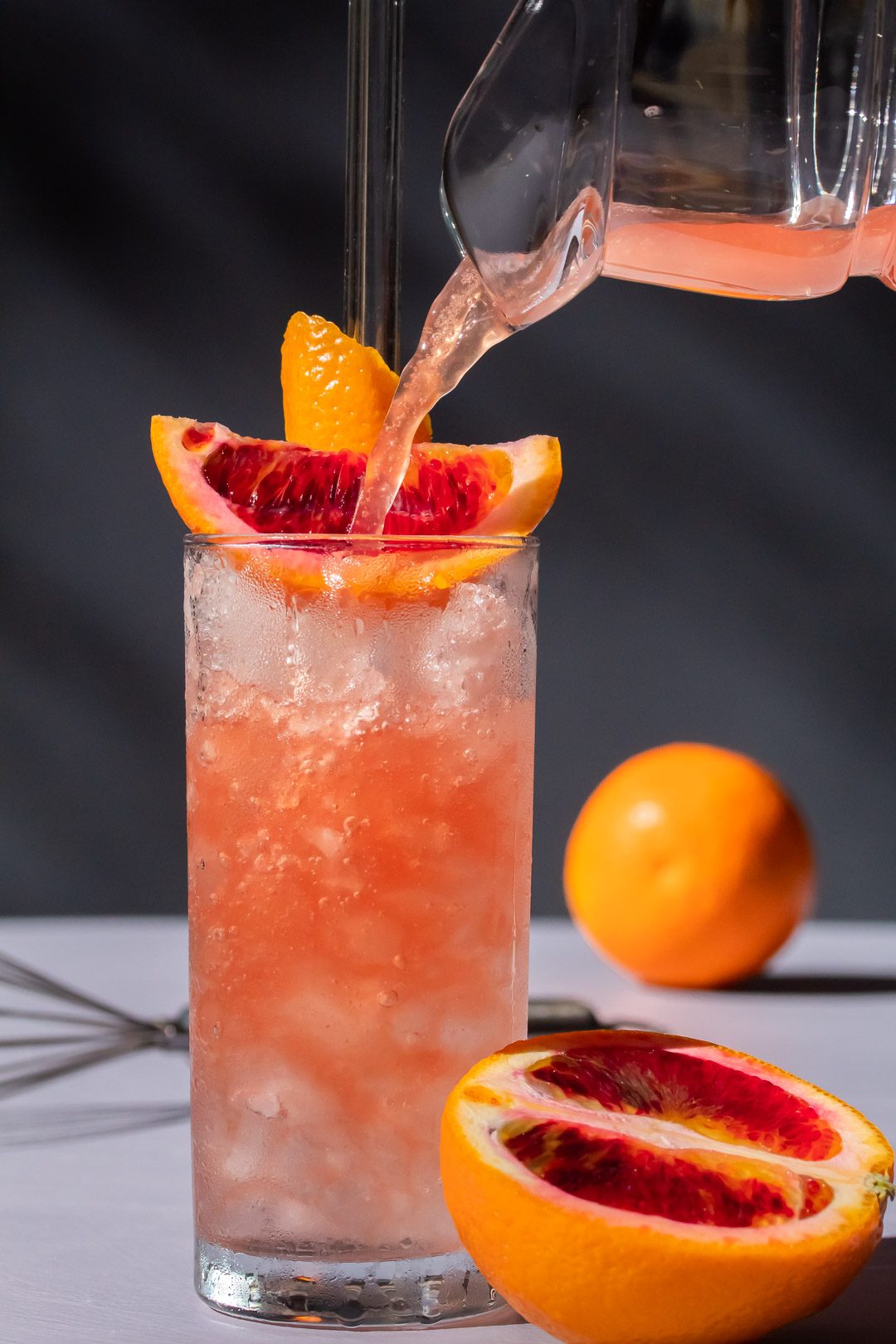 improved blood orangeade being poured into nearly full glass of crushed ice