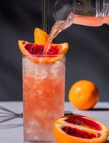 improved blood orangeade being poured into nearly full glass of crushed ice