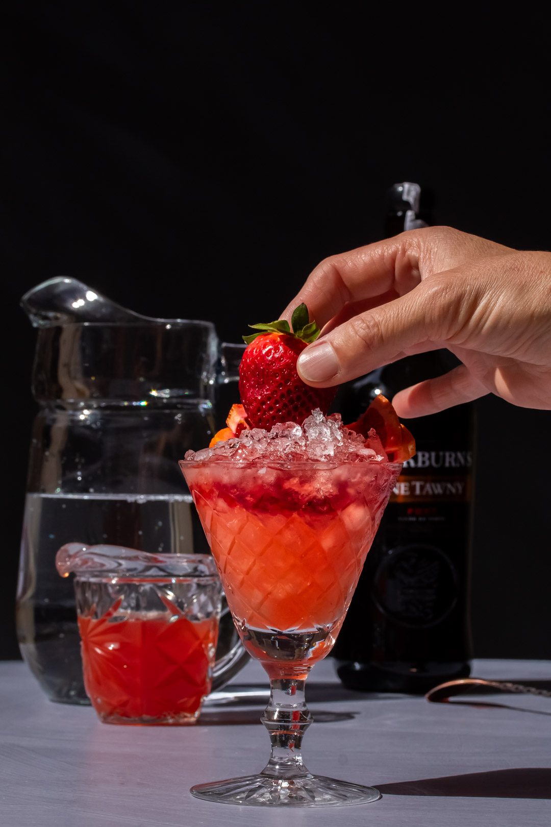 adding a fresh strawberry garnish to improved strawberry shrub