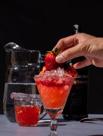 adding a fresh strawberry garnish to improved strawberry shrub