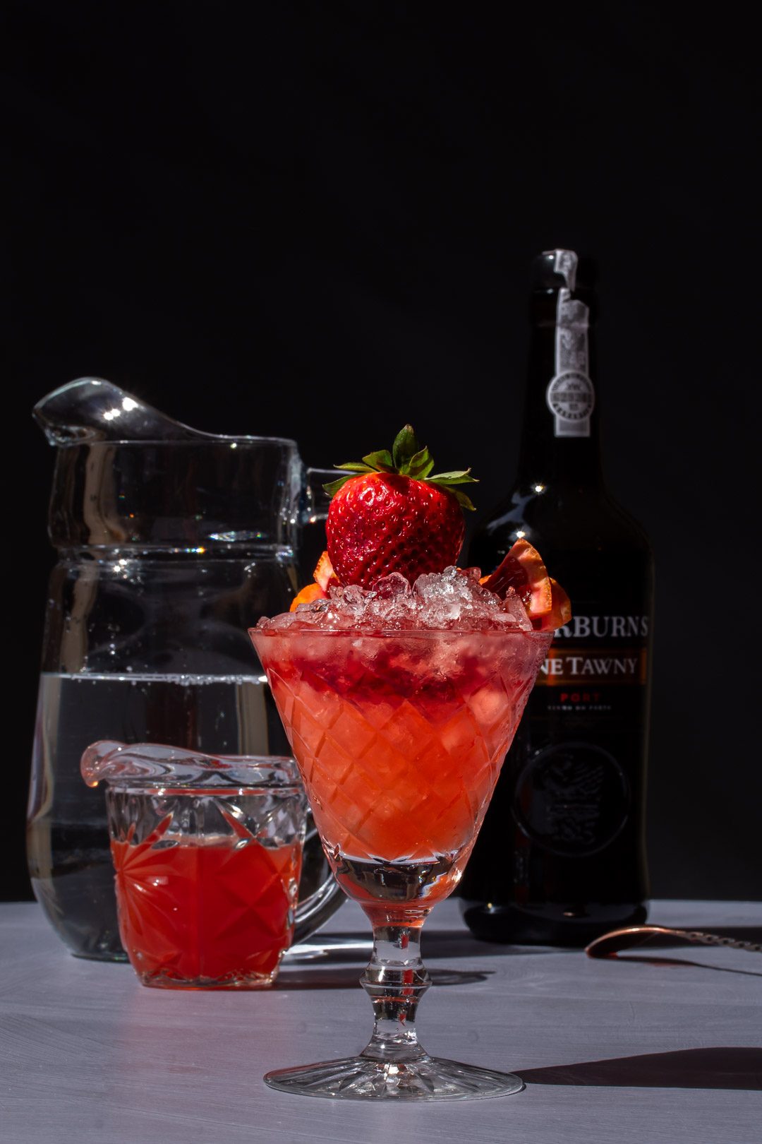 making an improved strawberry shrub port cocktail with bottles and jugs in background