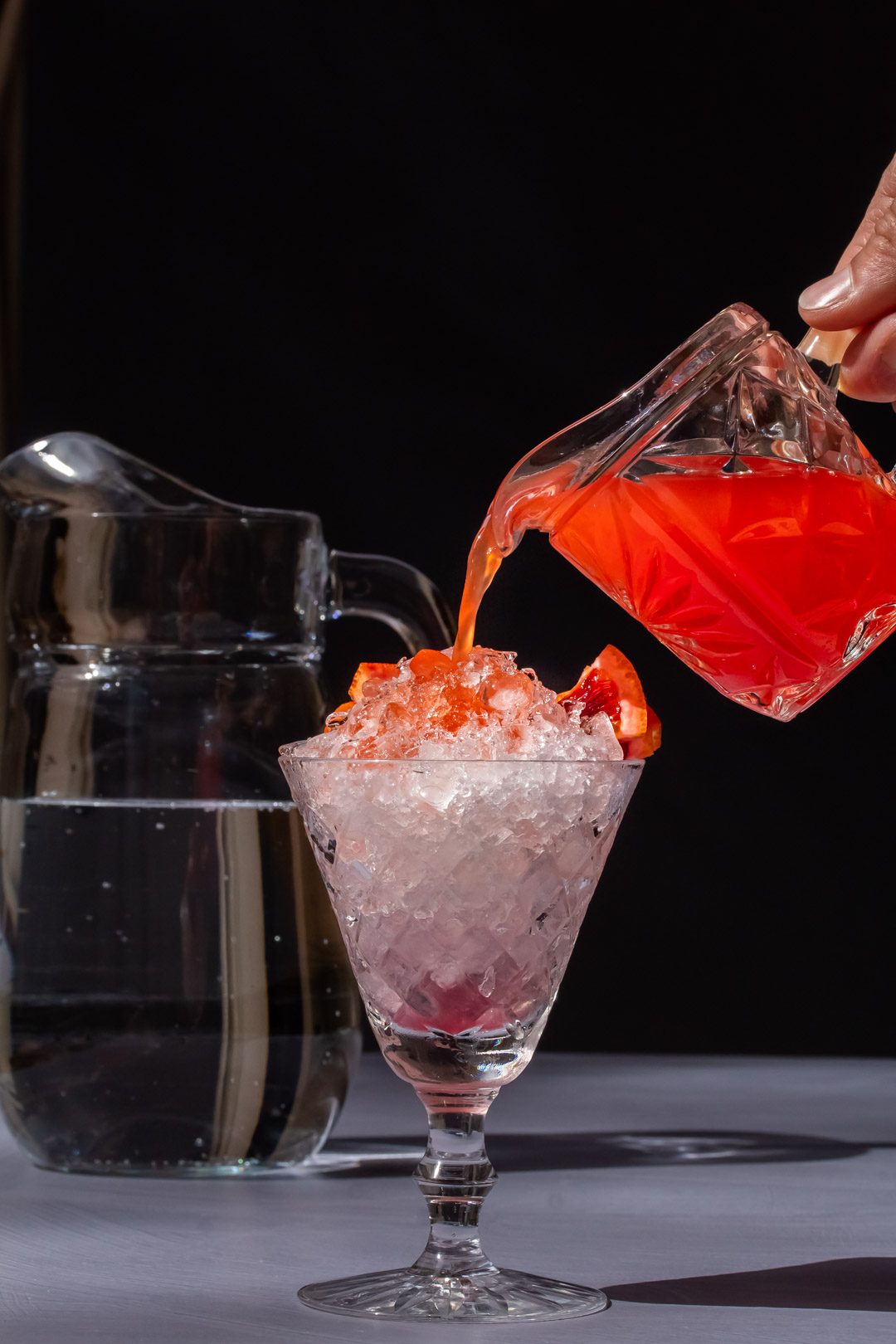 pouring improved strawberry shrub over crushed ice