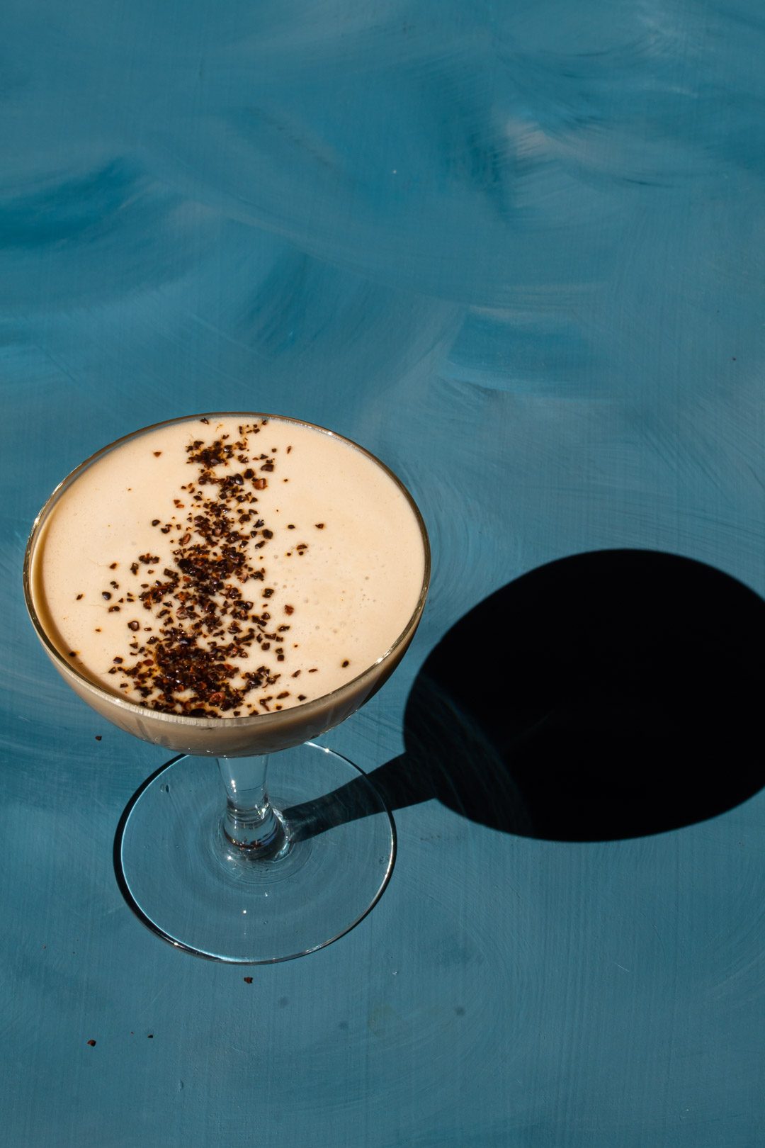 Quince Wattleseed Alexander Cocktail on blue background with shadow