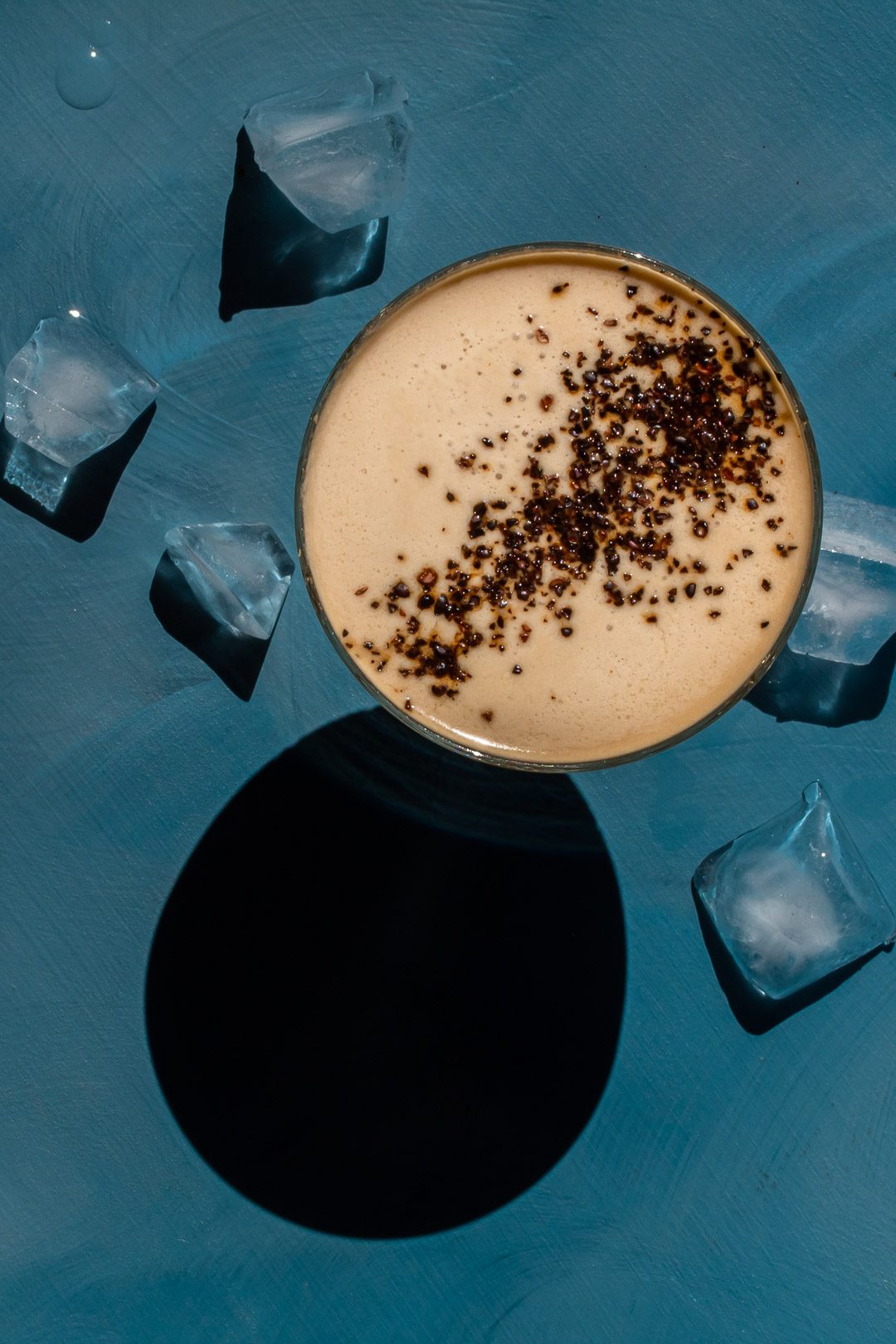 Quince Wattleseed Alexander Cocktail with ice on blue background