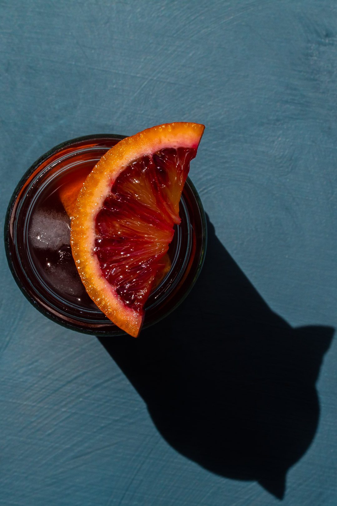 Pickle blood orange Americano cocktail from above on blue background with shadow