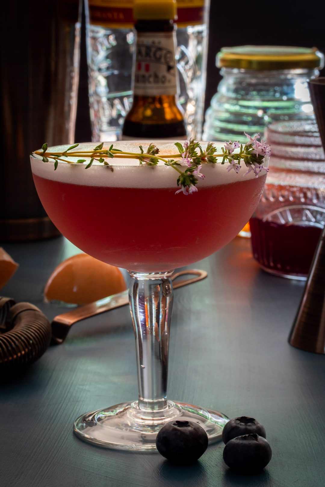 blueberry shrub pisco sour cocktail with bottles in background