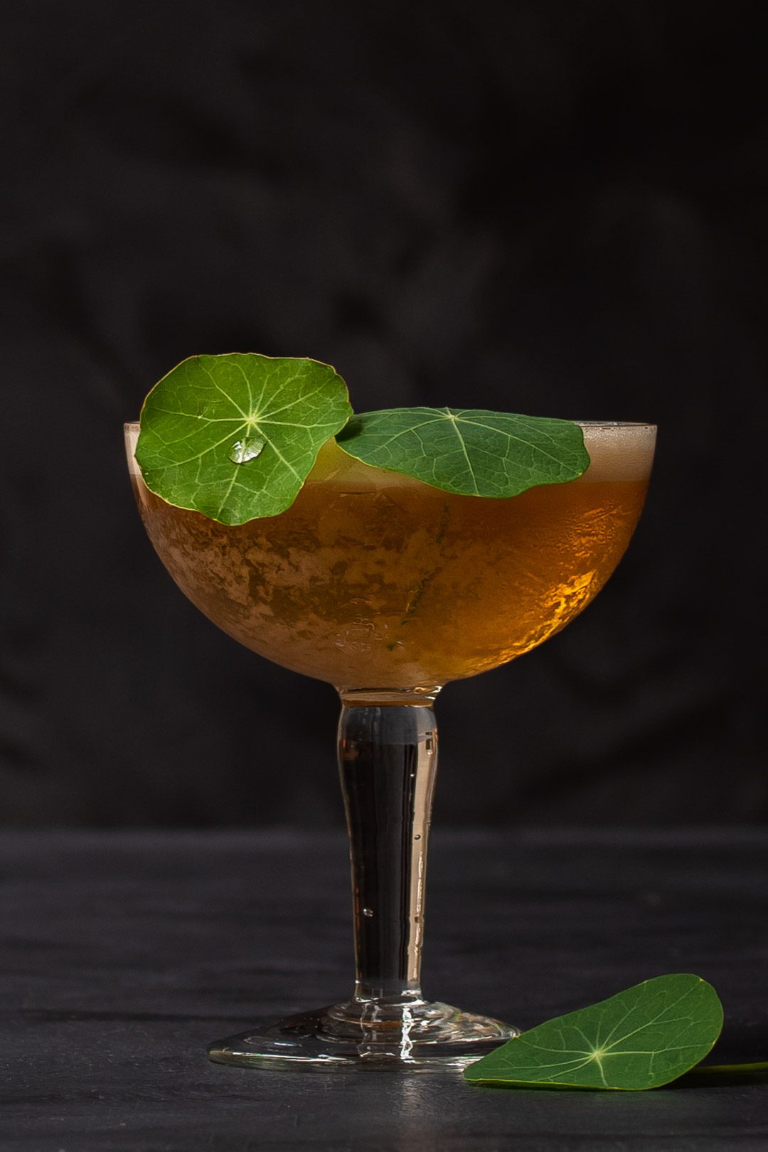 honey rhubarb silver sour with water drop on a nasturtium leaf garnish