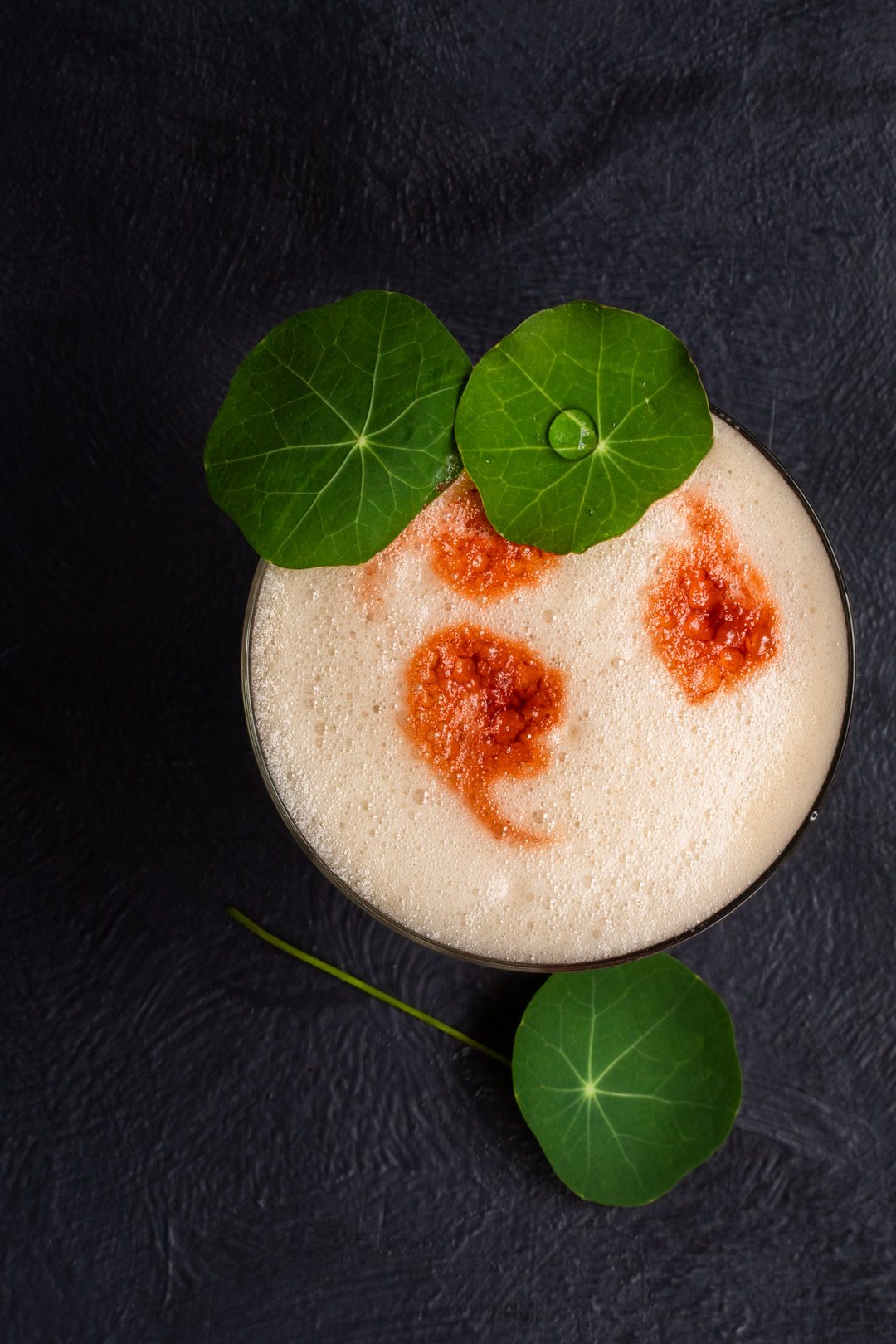 honey rhubarb silver sour from above with nasturtium leaf and water drop garnish