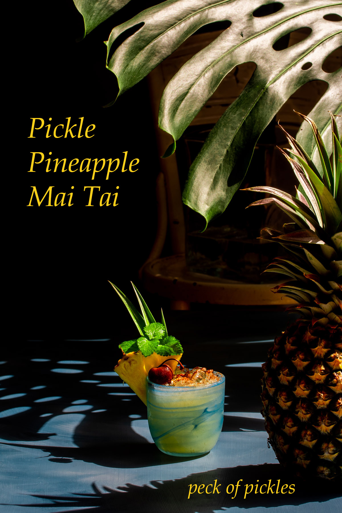 pickle pineapple shrub mai tai cocktail with pineapple in foreground and shadows in background