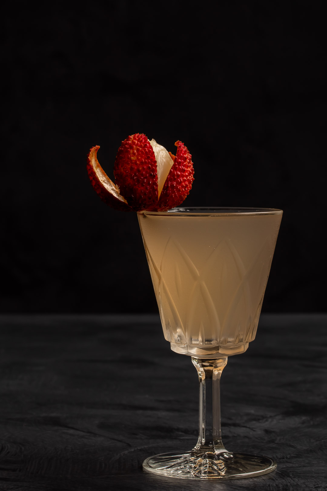 lychee reviver cocktail to right of frame with lychee garnish