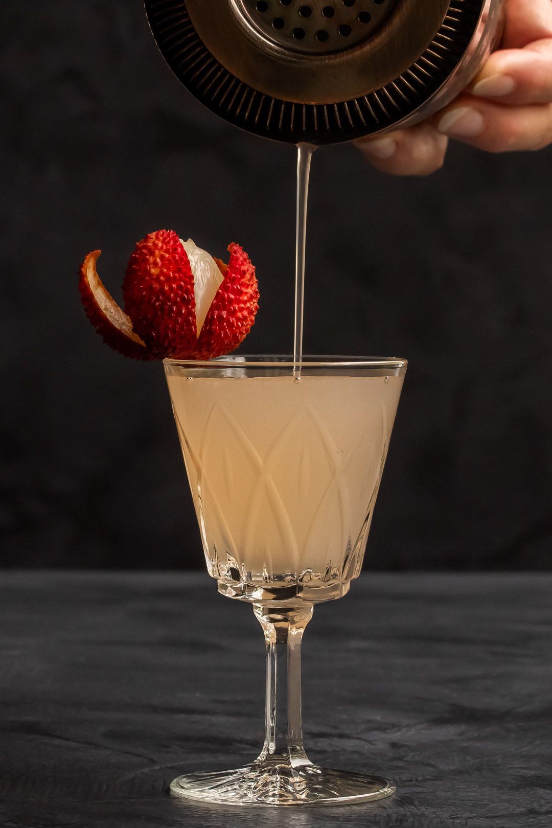 thin stream pouring lychee reviver cocktail with lychee garnnish