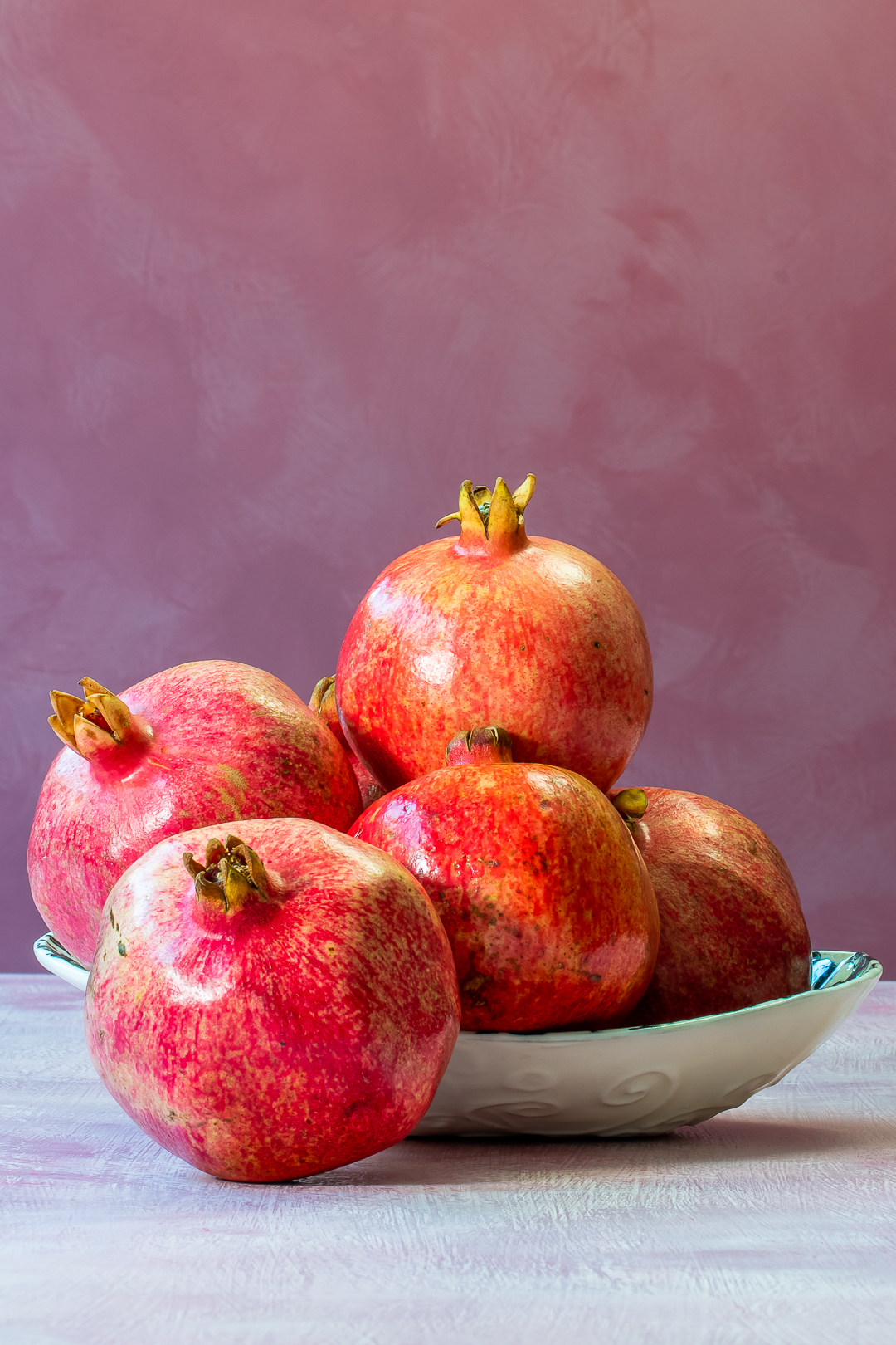 pomegranates in a dish for making grenadine on a pink background