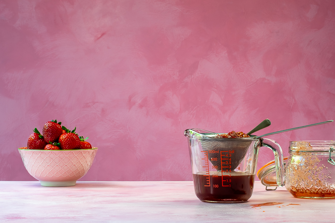 strained strawberry syrup in jug horizontal for making strawberry syrup for use in strawberry tequila collins