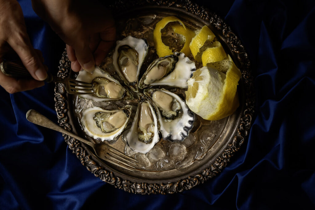 still life food art photo of scooping out a Sydney Rock Oyster with a fork using Baroque chiaroscuro lighting