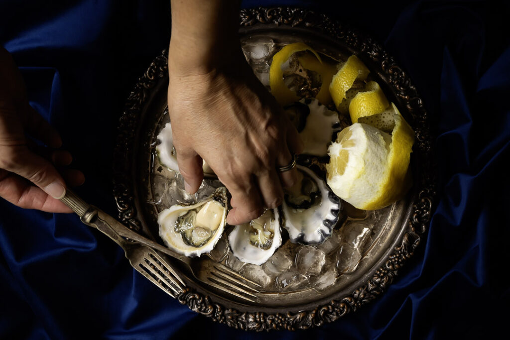 still life food art photo of a hand picking up a Sydney Rock Oyster using Baroque chiaroscuro lighting